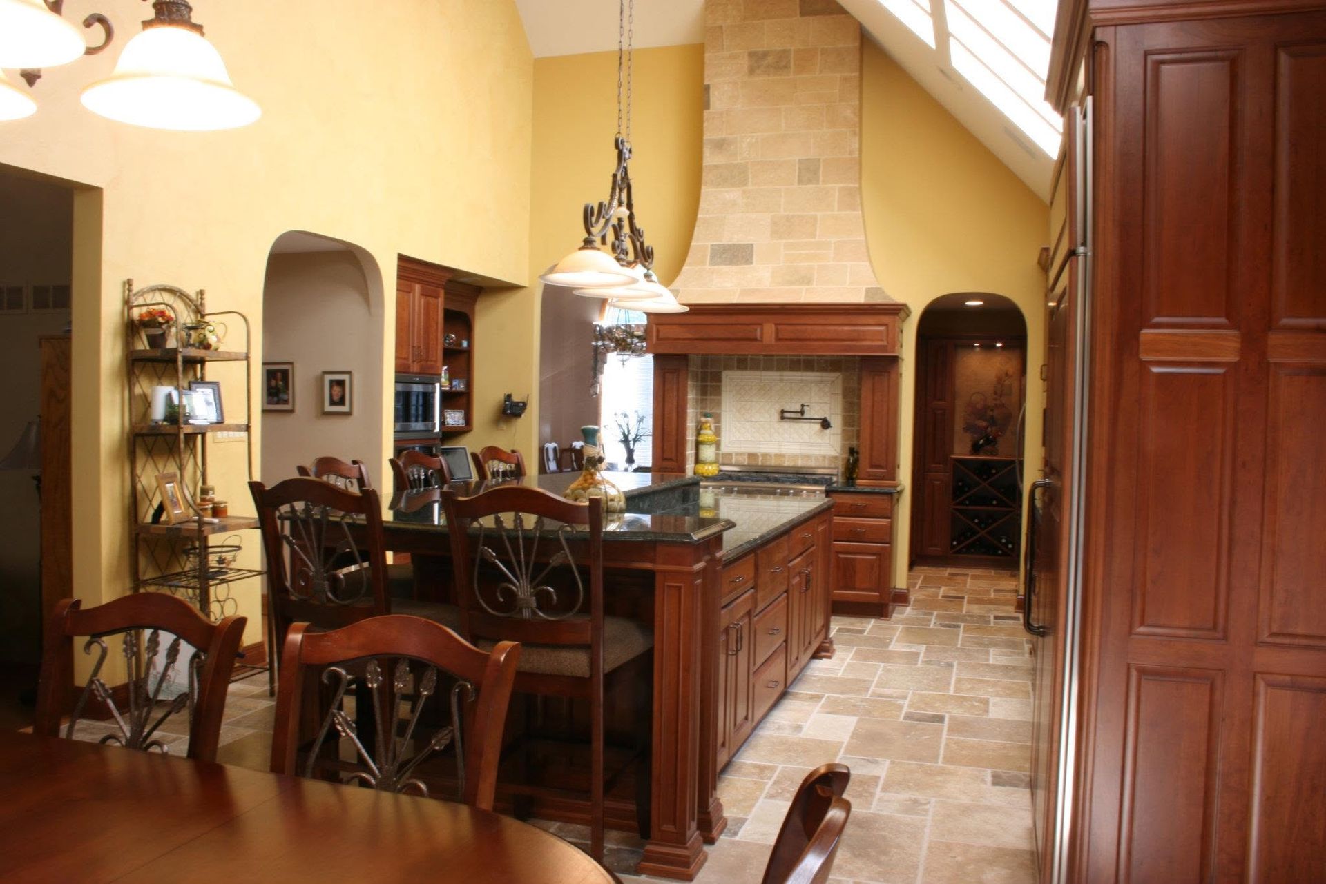 Warm kitchen with wood cabinets, island, and tiled floor in a yellow, cathedral-ceiling room