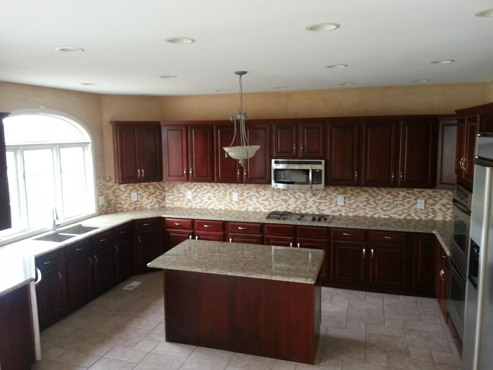 Spacious kitchen with dark wood cabinets, granite island, mosaic backsplash, and large window.