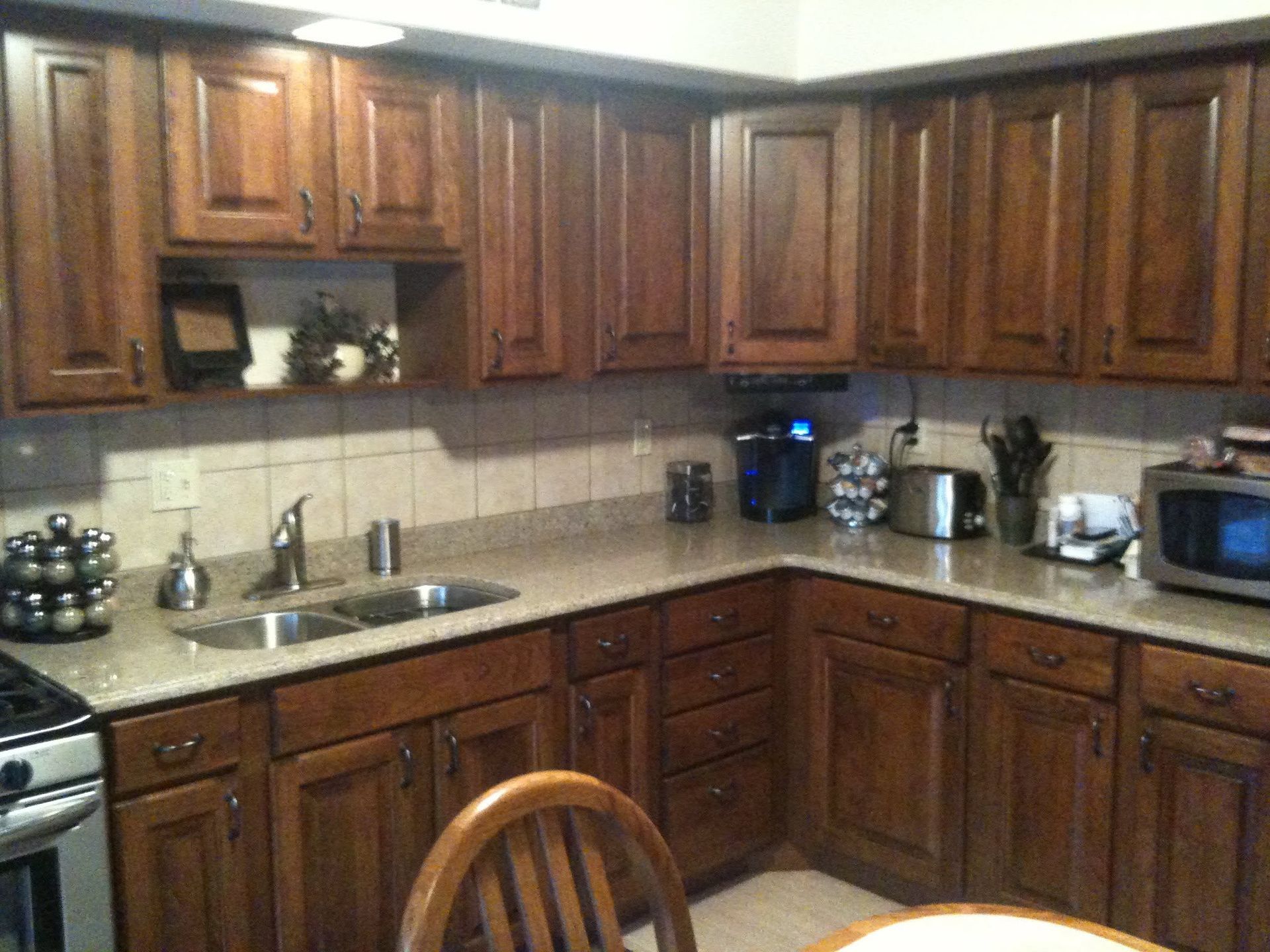 Wooden kitchen with dark cabinets, beige countertops, sink, appliances, and a wooden chair in the foreground