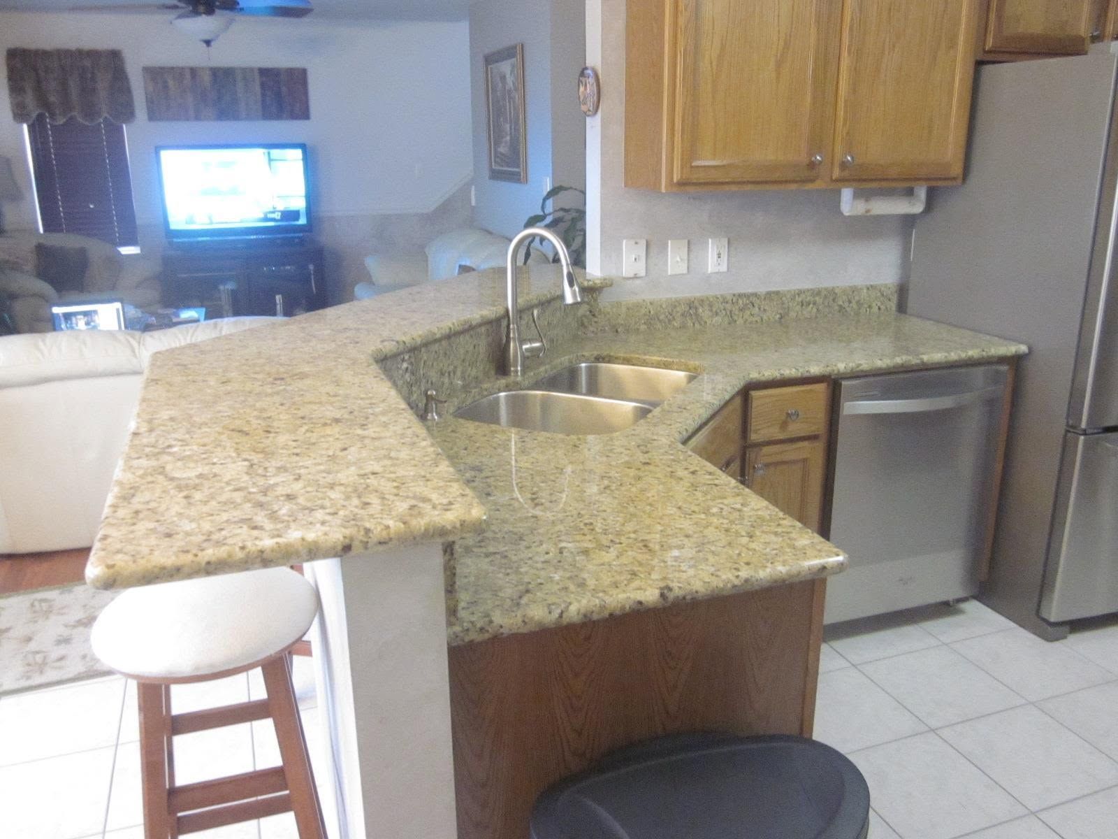Kitchen with granite island, stainless sink, white tile floor, and view into a living room.