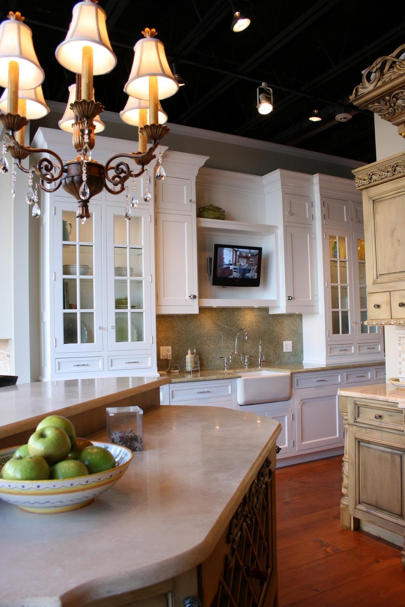 Modern kitchen with white cabinets, wood island, hanging chandelier, and bowl of green apples
