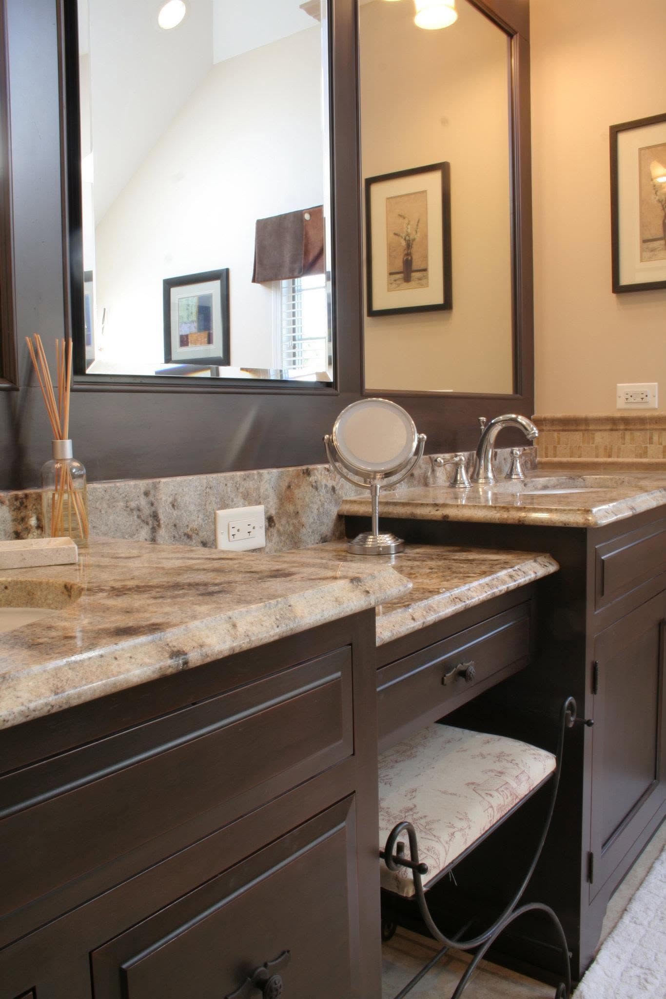 Bathroom vanity with granite countertop, mirror, sink, and makeup items in warm lighting