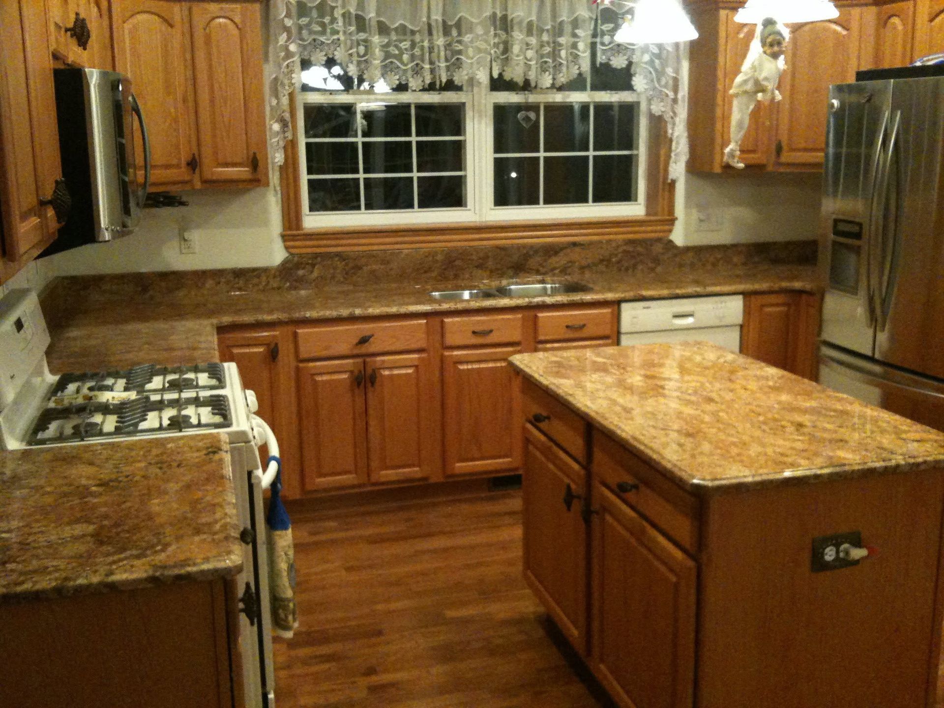 Wooden kitchen with granite counters, island, gas stove, stainless fridge, and a window over the sink.