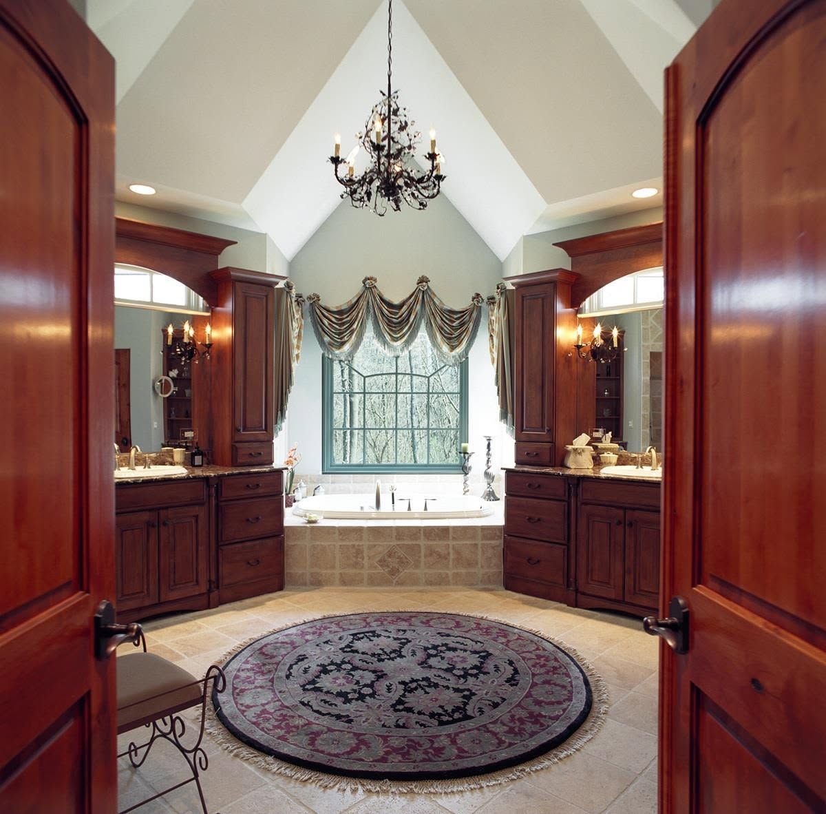 Elegant bathroom with wood cabinets, a chandelier, large window, and round rug in the center