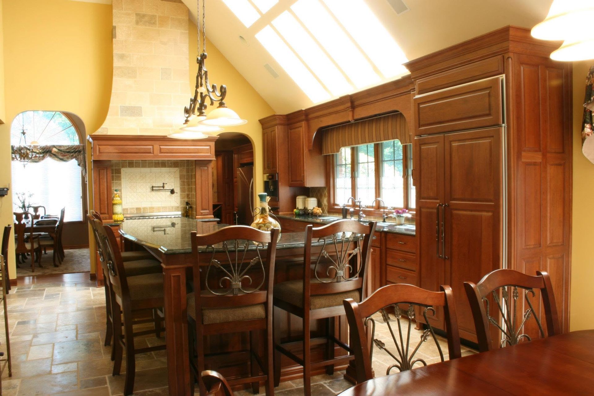 Elegant wood-paneled kitchen and dining area with long table, chairs, and skylight lighting
