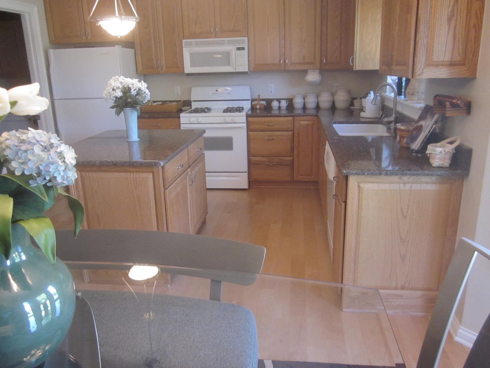 Kitchen with wooden cabinets, white appliances, and a dining table with blue flowers.