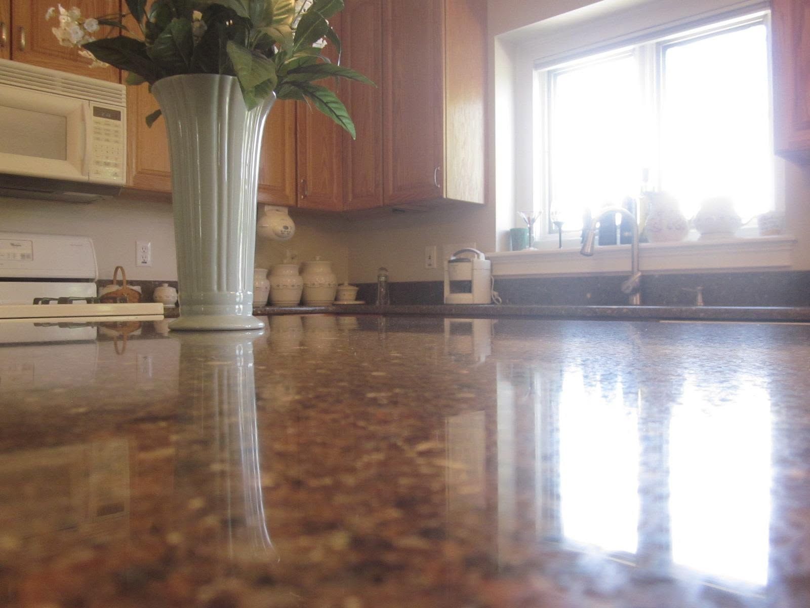 Kitchen countertop with a vase of flowers, reflecting a bright window and cabinets in the background