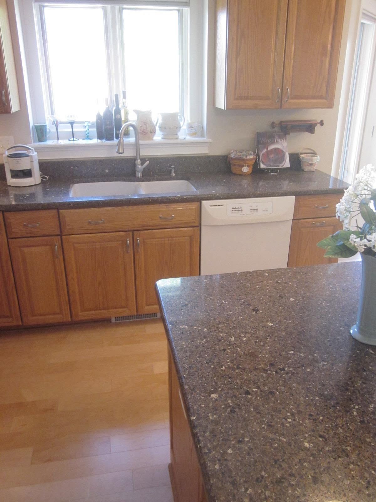 Kitchen with wooden cabinets, granite countertops, sink, and dishwasher near a bright window.