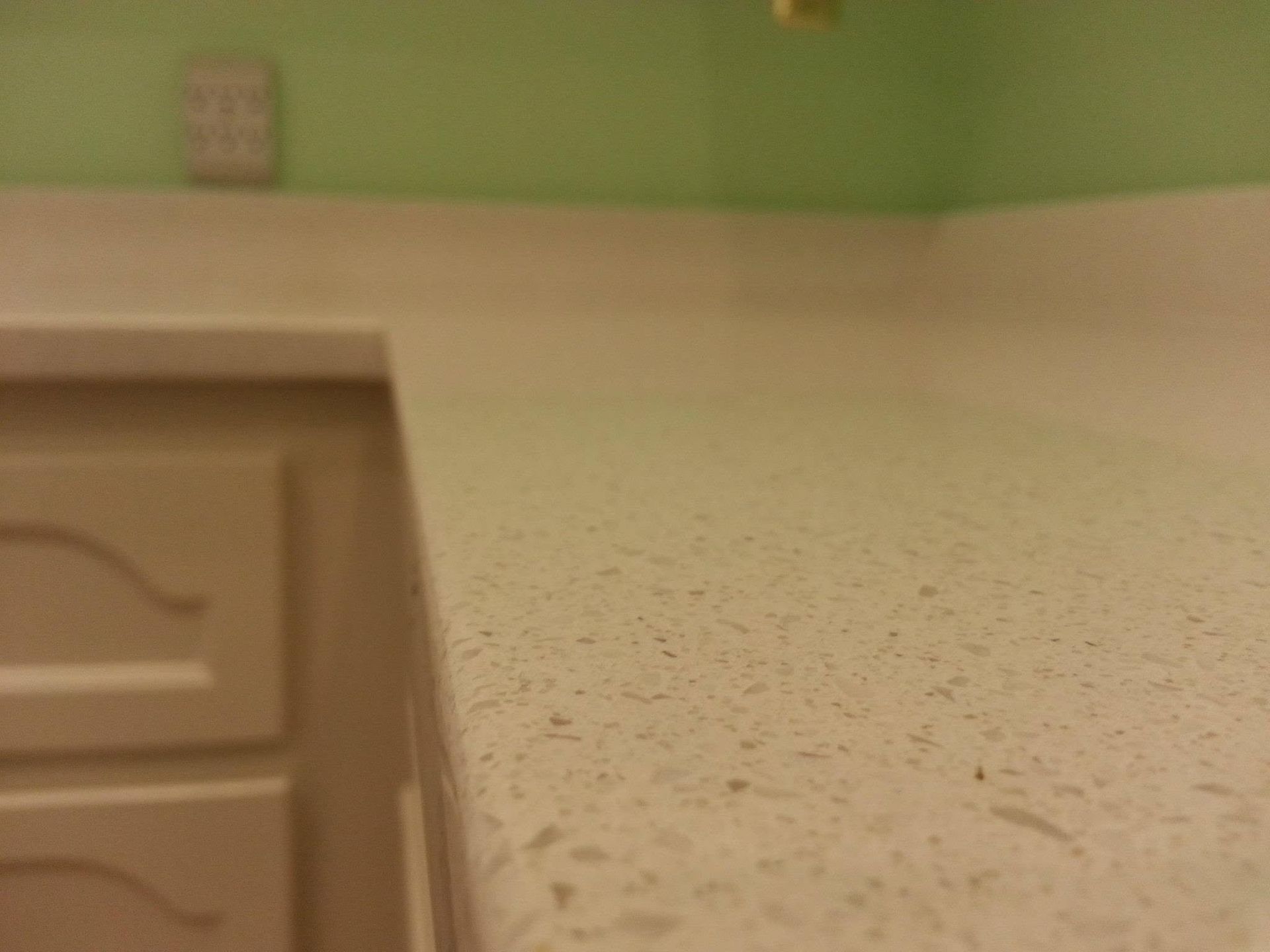 Indoor countertop corner with beige speckled surface, green wall, and part of a cabinet drawer.