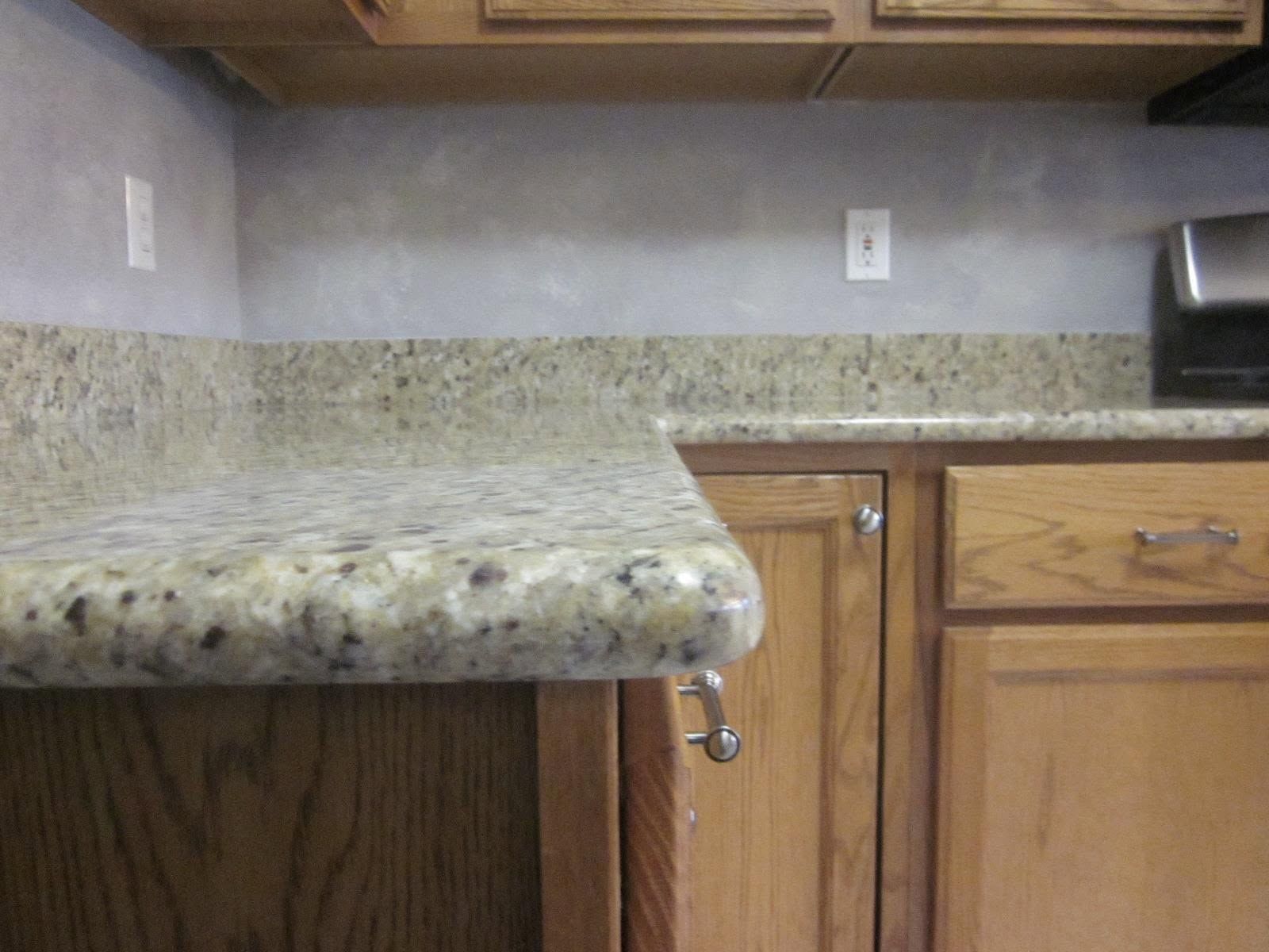 Kitchen countertop with speckled granite, light wood cabinets, and a black microwave in the corner.