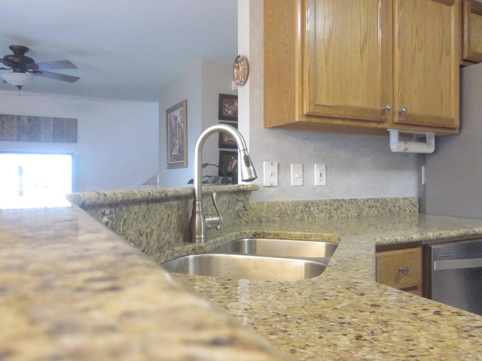 Kitchen with granite countertop, stainless sink, and wooden cabinets in a bright open interior.