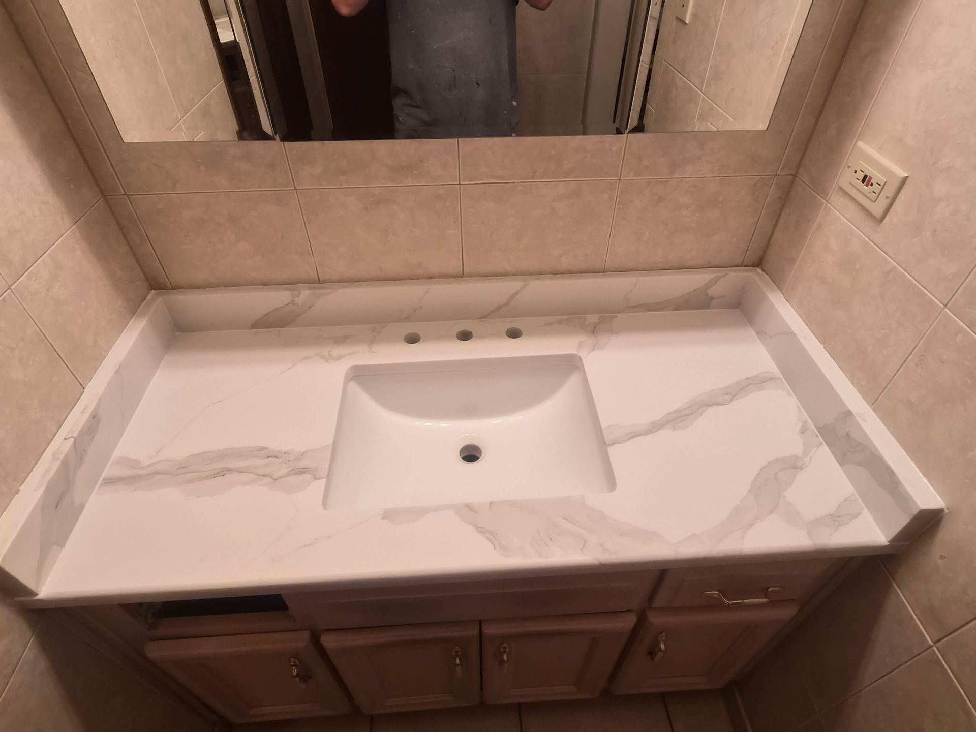 Bathroom vanity with marble countertop, built-in sink, and mirror above wooden cabinets.