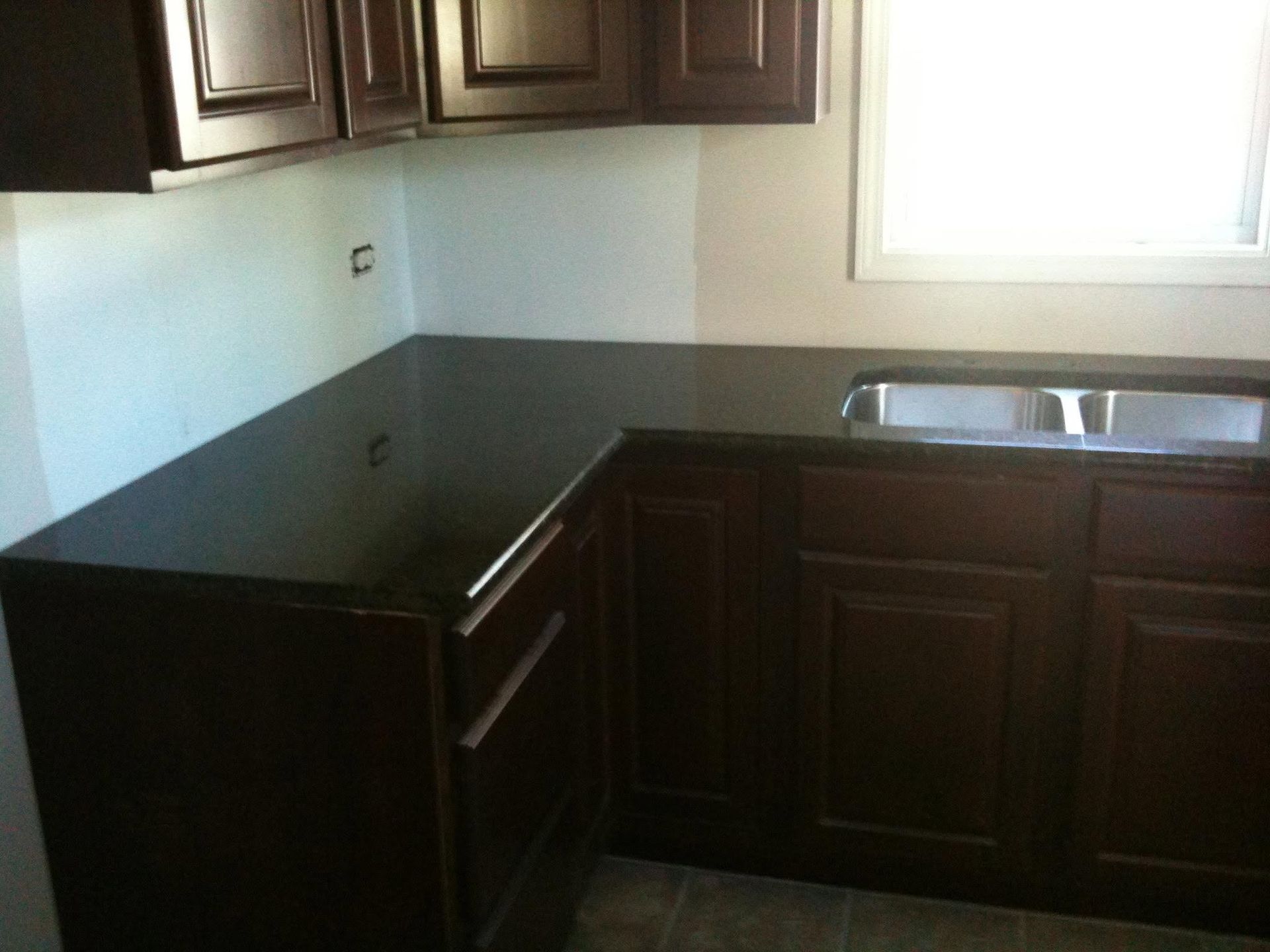 Empty kitchen with dark wood cabinets, black countertops, and a double sink under a window