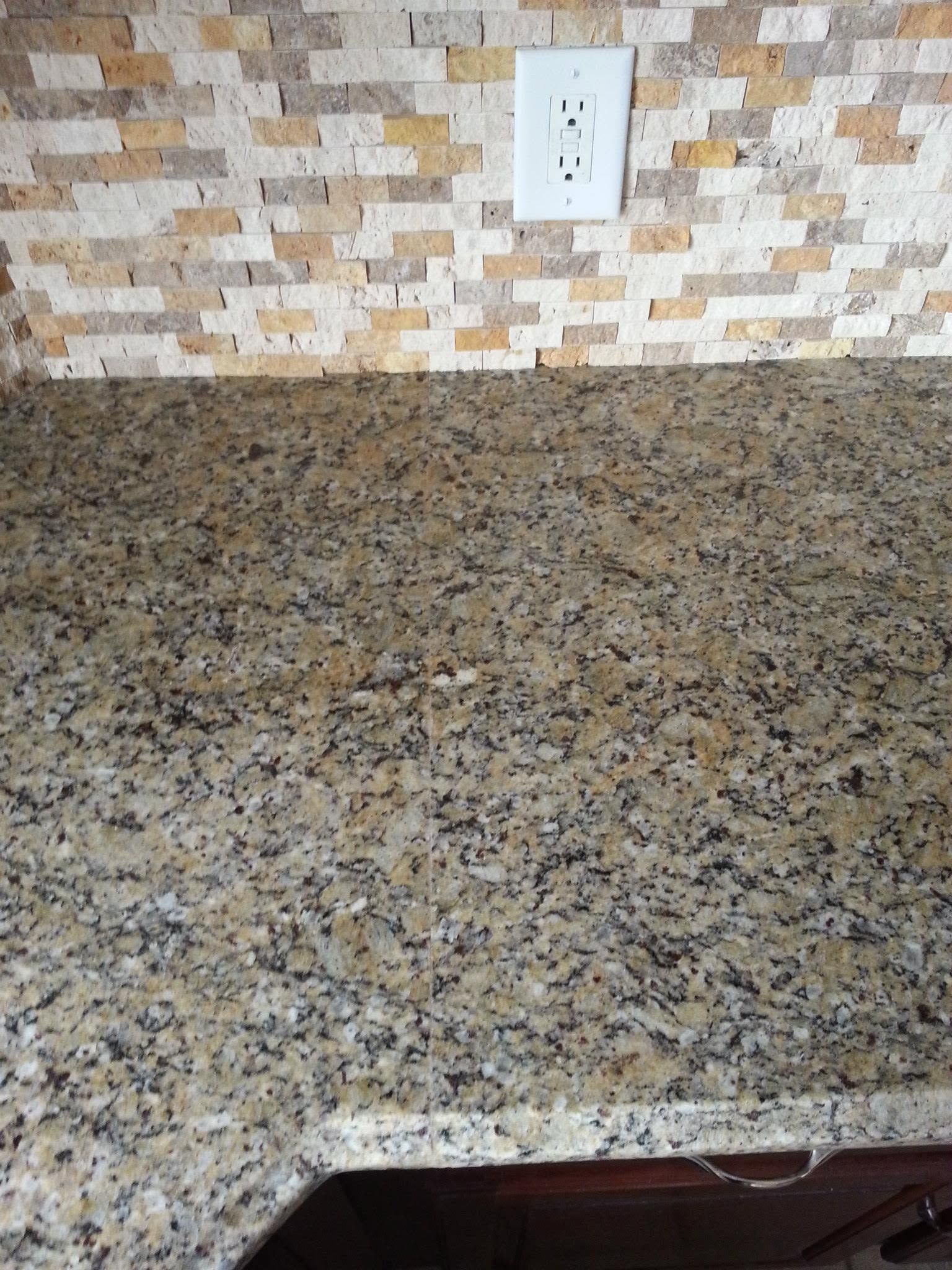 Speckled granite kitchen countertop with tiled backsplash and electrical outlet