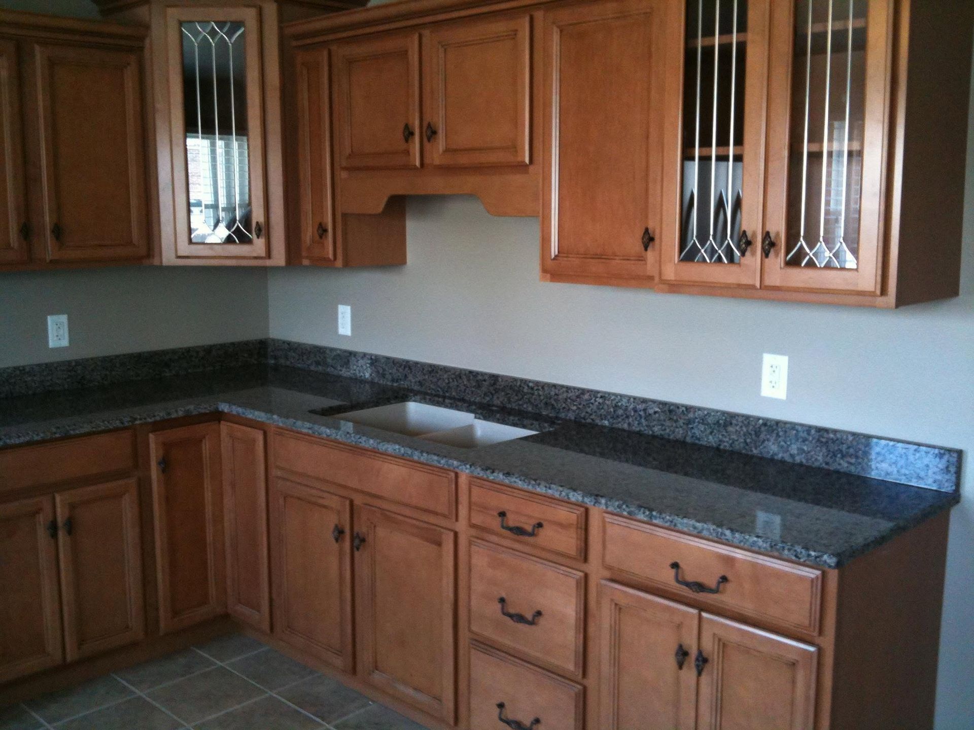Empty kitchen with dark granite countertops and honey-colored cabinets under glass-front upper cabinets