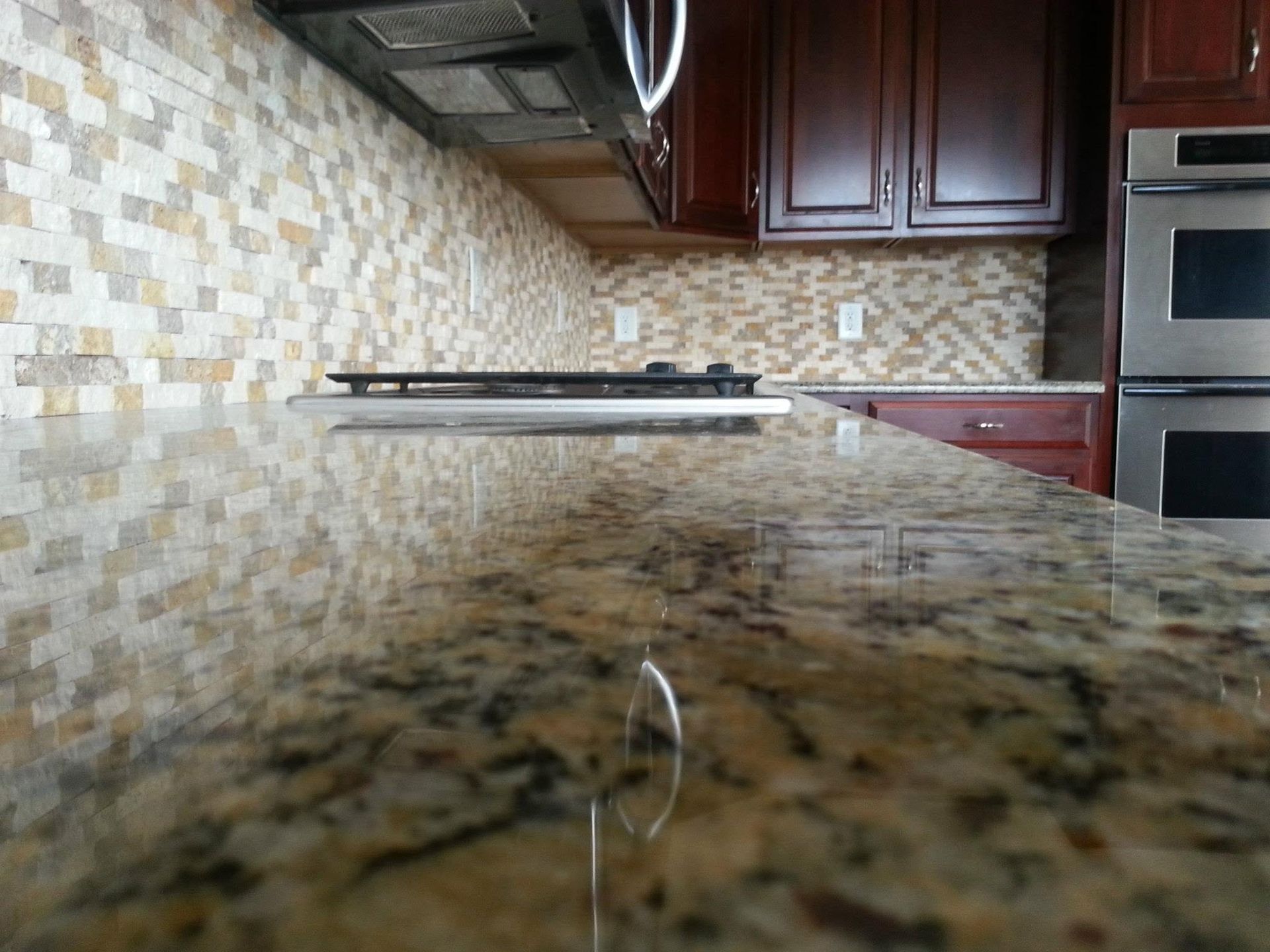 Kitchen countertop with granite surface, tiled backsplash, dark cabinets, and built-in oven.