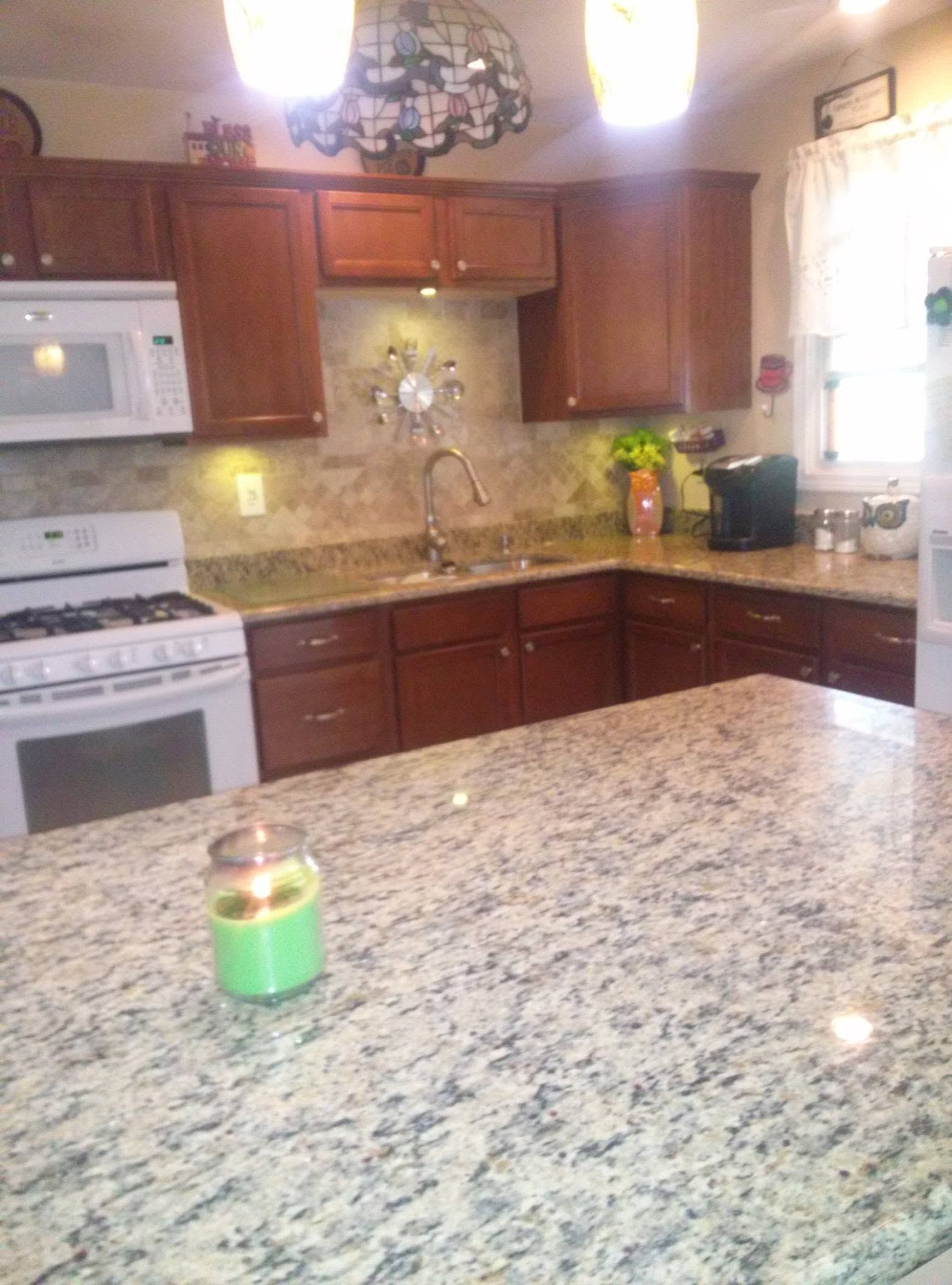 Modern kitchen with wooden cabinets, granite island, white stove, and green candle on the counter.