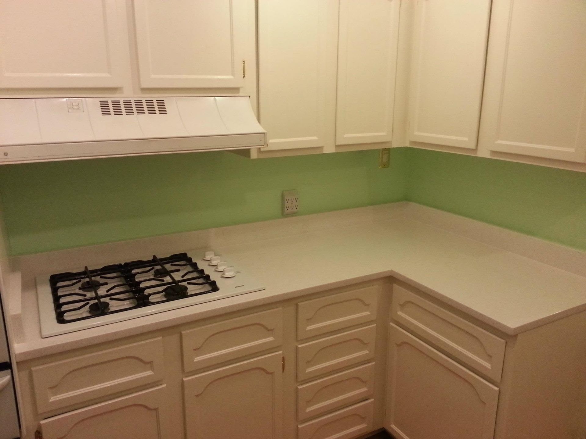 Small kitchen with white cabinets, green walls, and a gas stove under a white range hood.