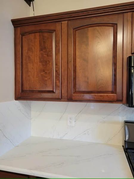 Wooden kitchen cabinets above a white countertop and marble-look backsplash