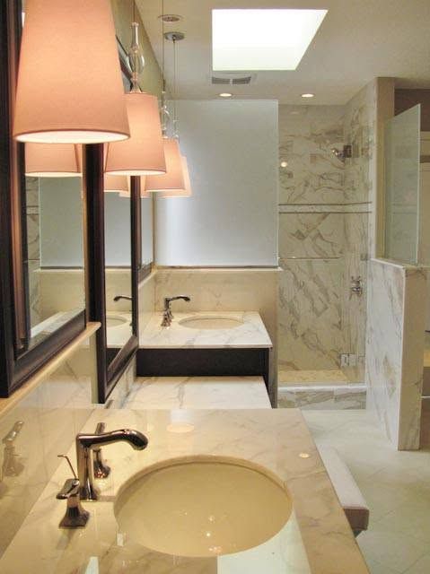 Modern bathroom with double sinks, large mirrors, marble walls, and a bathtub in the back.