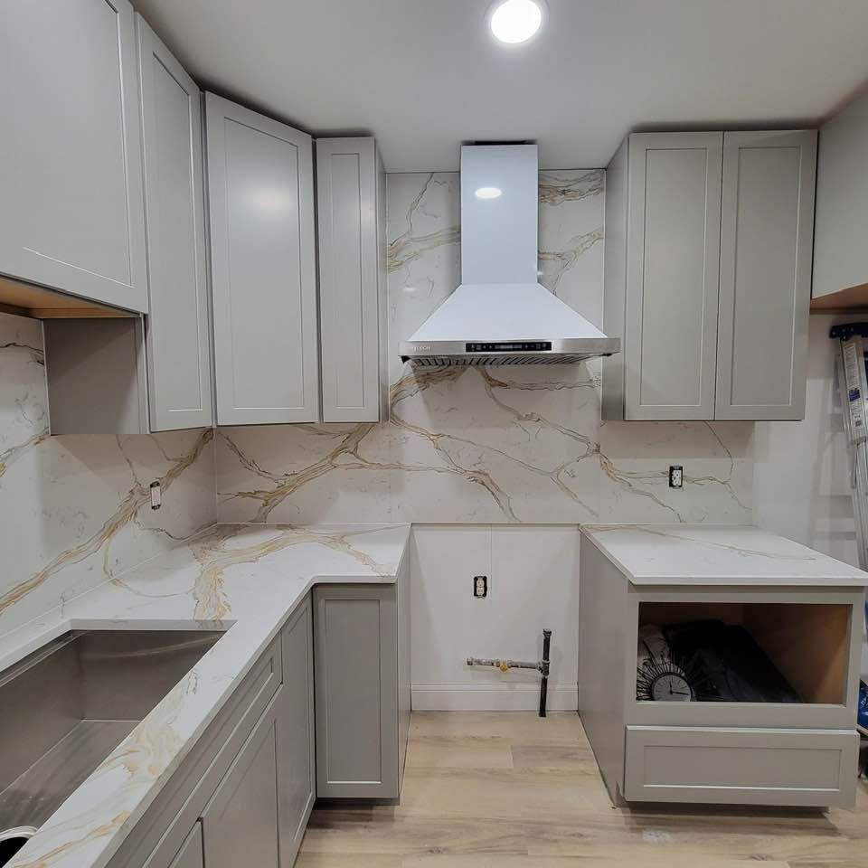 Modern white kitchen with marble-look backsplash, gray cabinets, and a central range hood