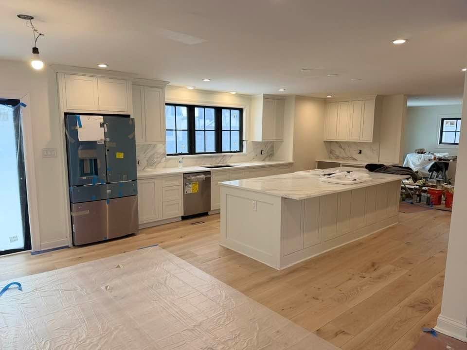 Bright modern kitchen with white cabinets, island, stainless fridge, and light wood floors