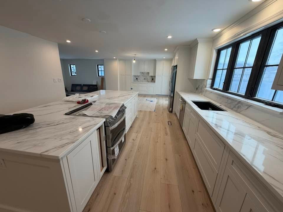 Bright, modern kitchen with white cabinets, marble countertops, and a long island with stainless appliances.