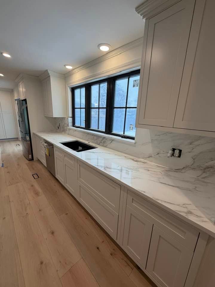 Bright modern kitchen with white cabinets, marble countertop, black sink, and large window over wooden floors