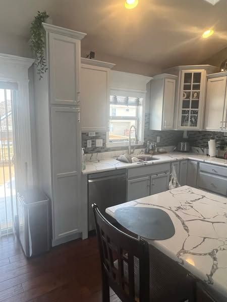 Bright kitchen with white cabinets, dark dishwasher, marble-pattern island, and hardwood floor.