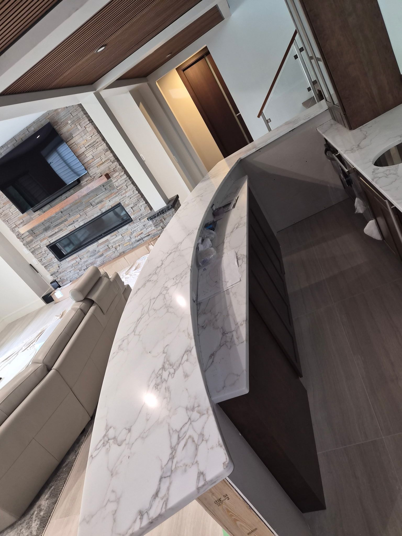 Modern kitchen with marble island, dark cabinets, and beige seating, viewed at an angle