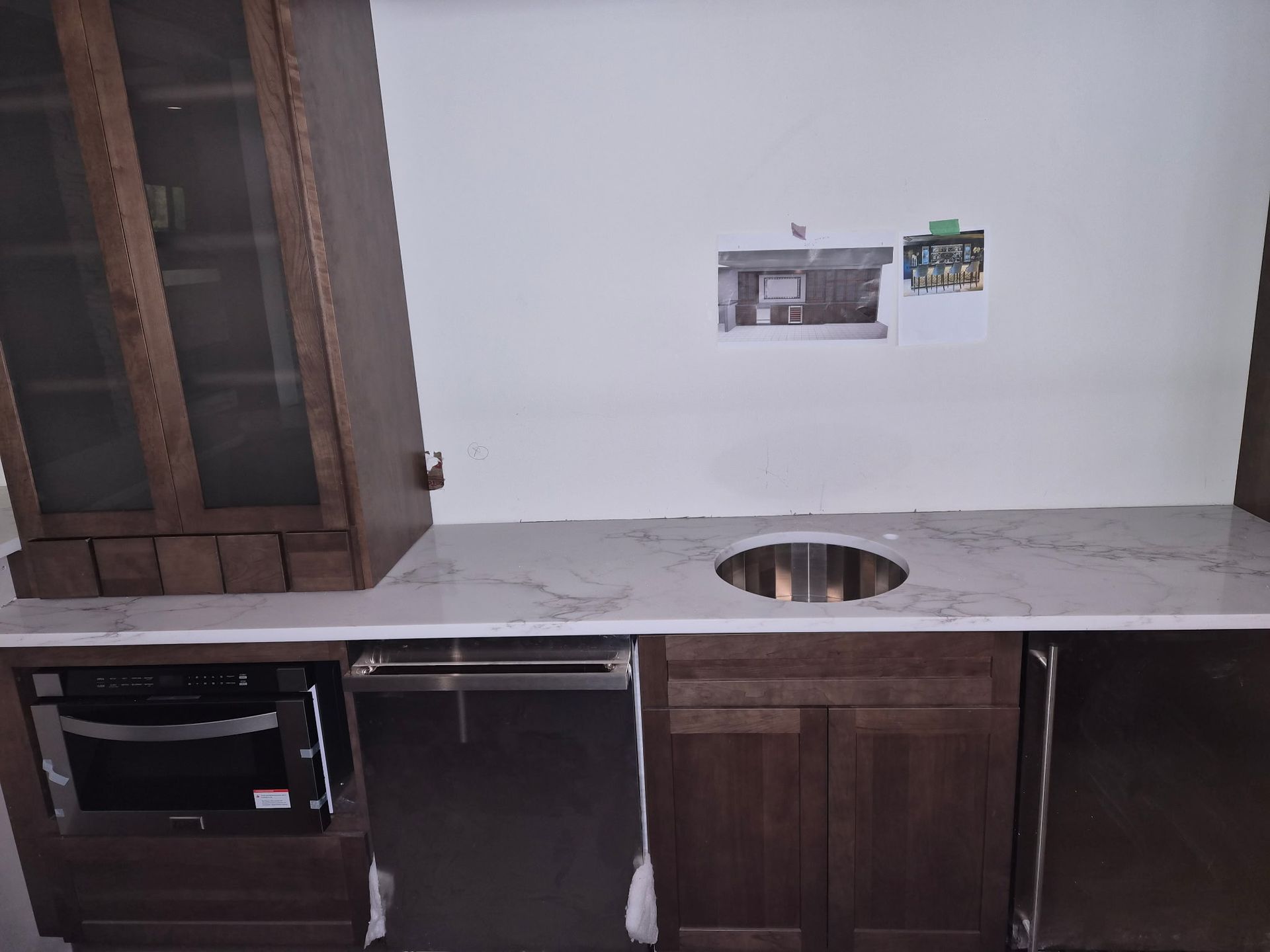 Unfinished kitchen with marble countertop, sink cutout, dark wood cabinets, and exposed appliance spaces