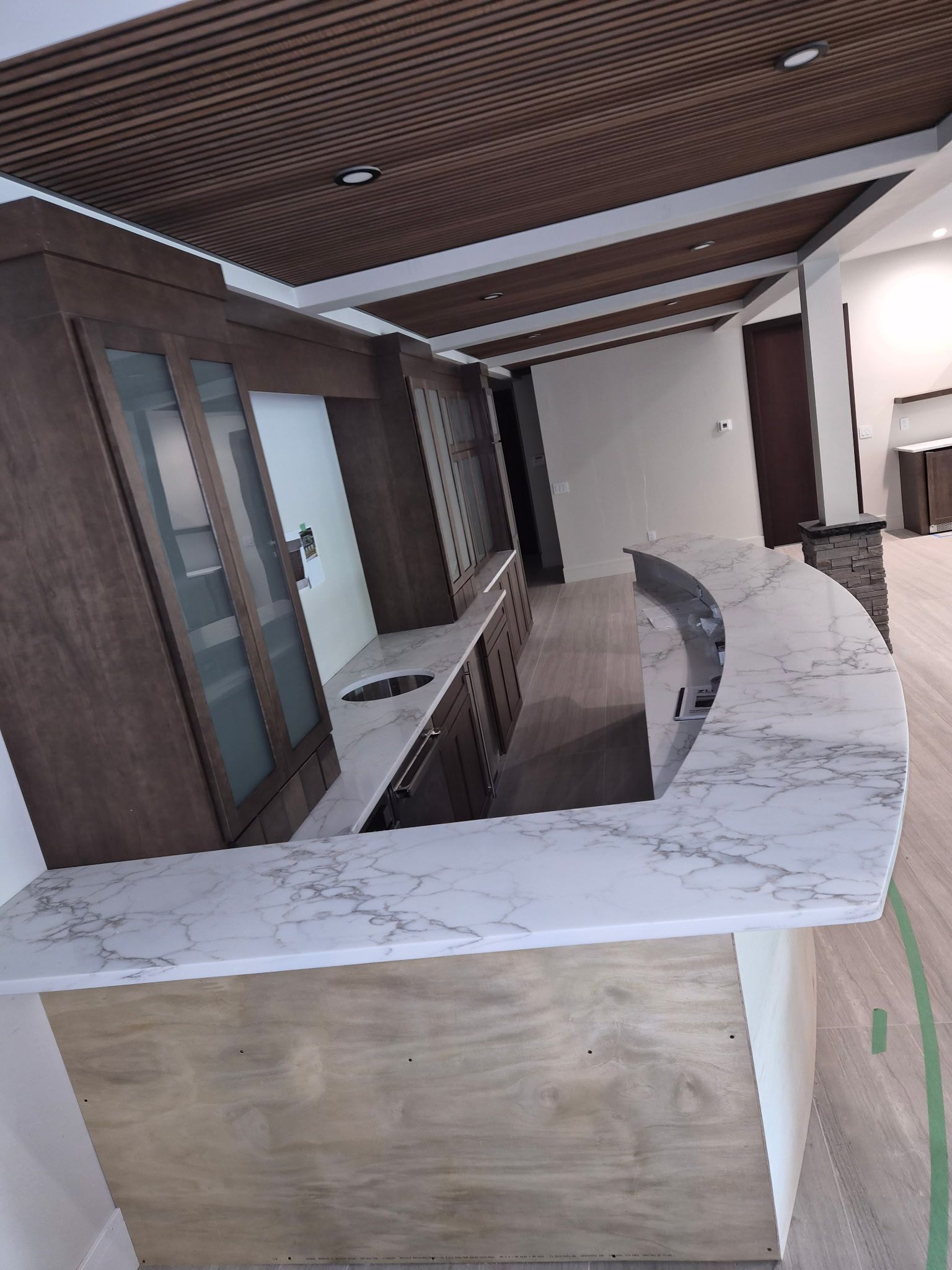Curved marble reception counter in a modern office lobby with wood ceiling and glass doors.