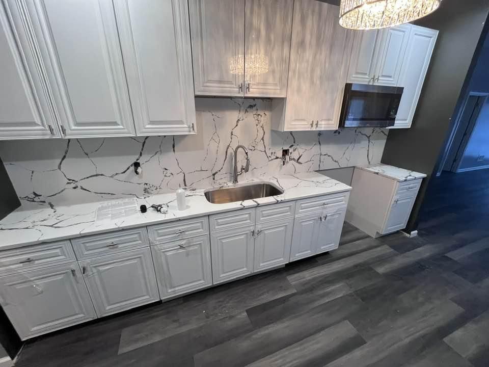 Modern kitchen with white cabinets, marble-look backsplash, stainless sink, and dark gray wood flooring.