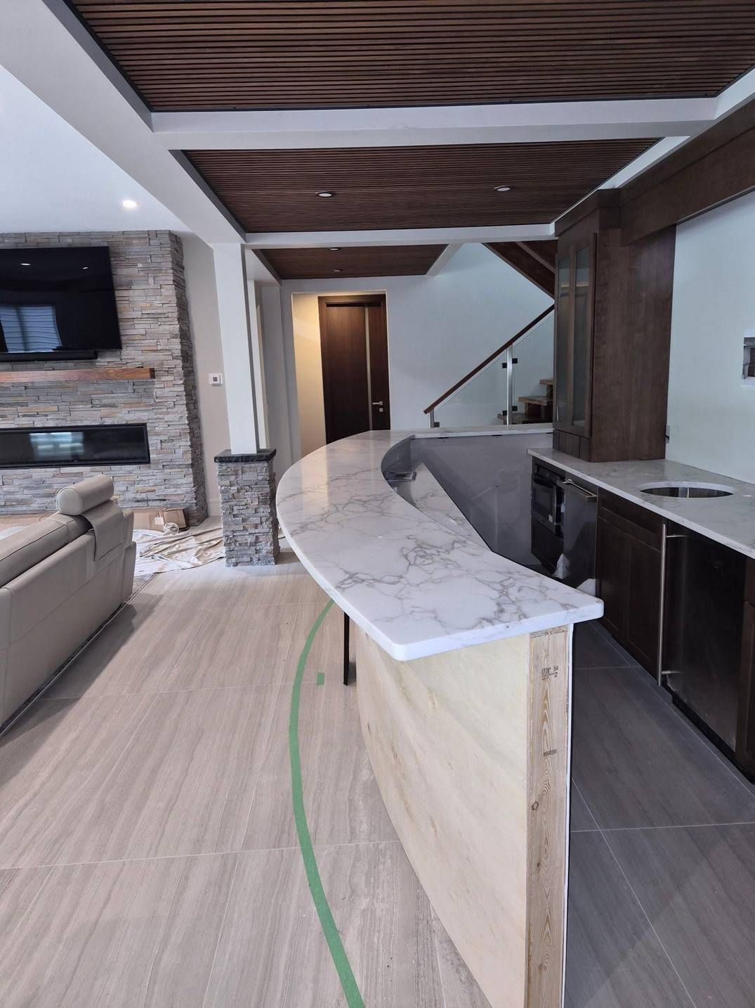 Modern living room with curved stone bar, wood ceiling, fireplace, and staircase