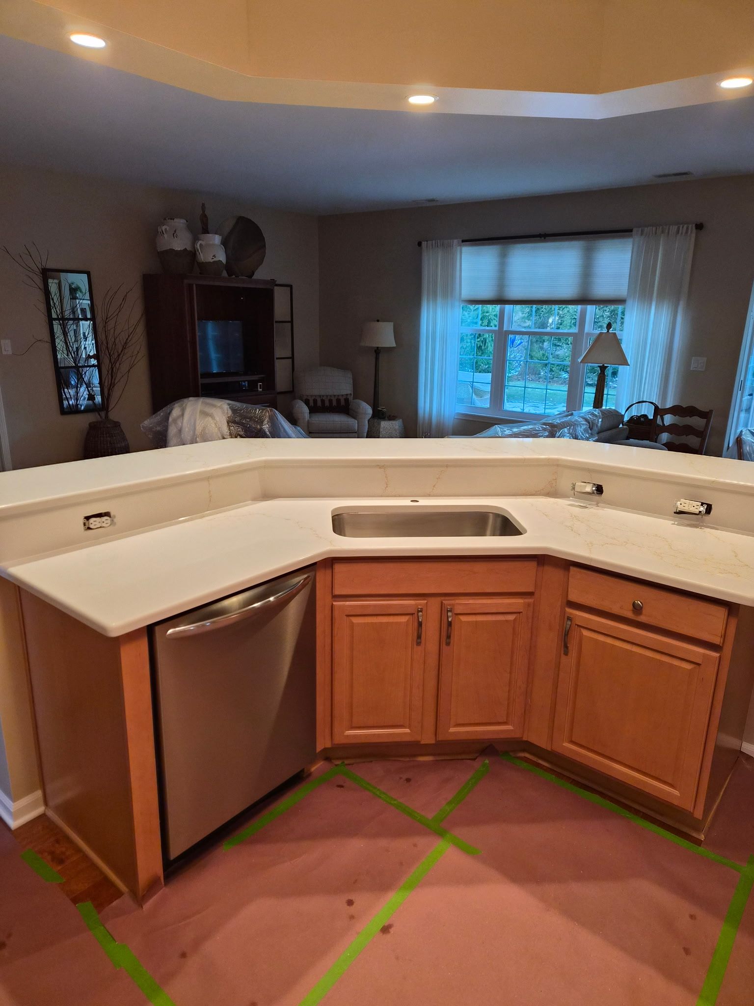 Kitchen with white countertop peninsula, wood cabinets, stainless dishwasher, and green tape marking the floor.
