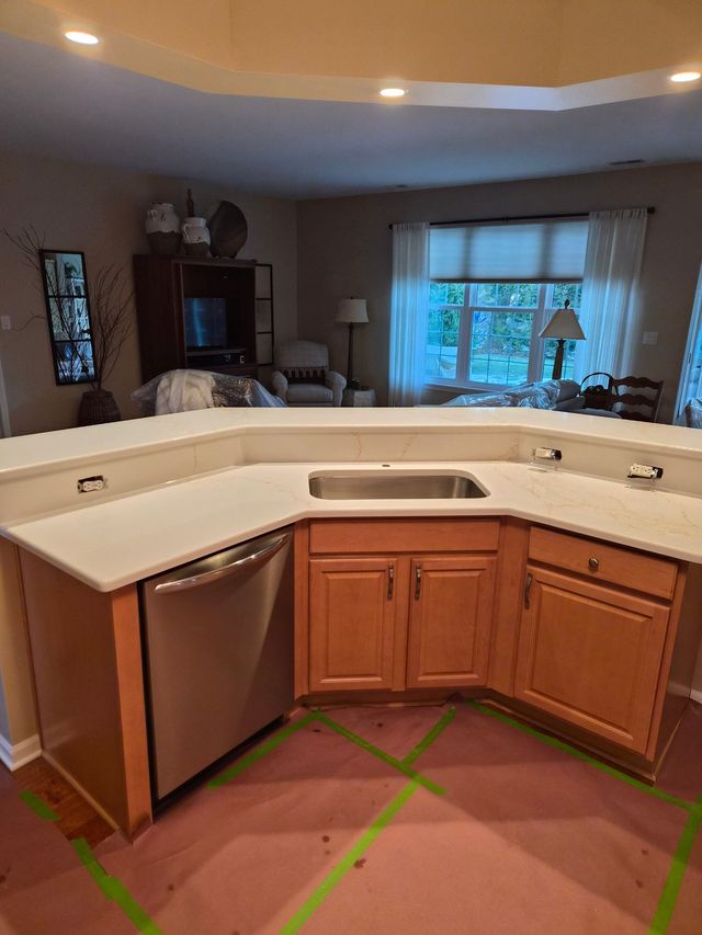 Kitchen with white countertop peninsula, wood cabinets, stainless dishwasher, and green tape marking the floor.
