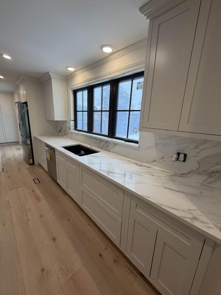 Modern kitchen with white cabinets, marble countertop, and large black-framed windows.