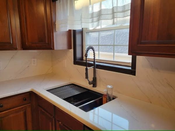 Modern kitchen sink with black faucet, white countertop, and wood cabinets by a window