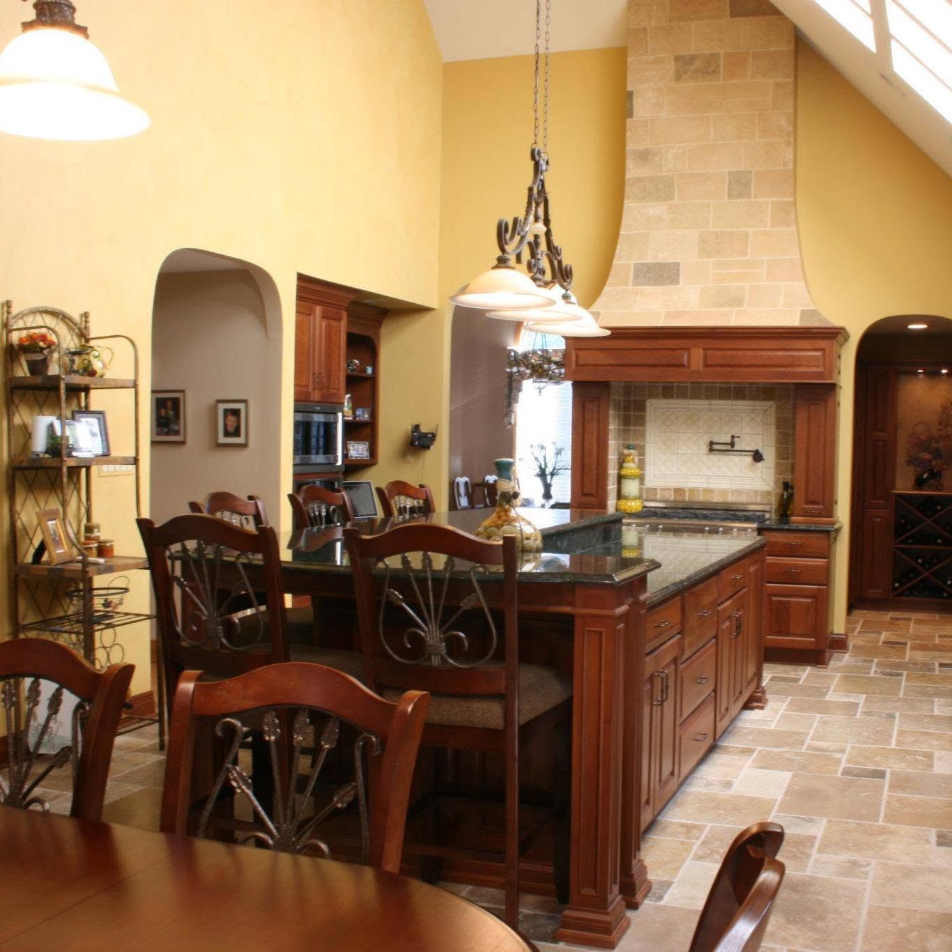 Warm kitchen with dark wood island, tiled floor, hanging lights, and a stone fireplace alcove.