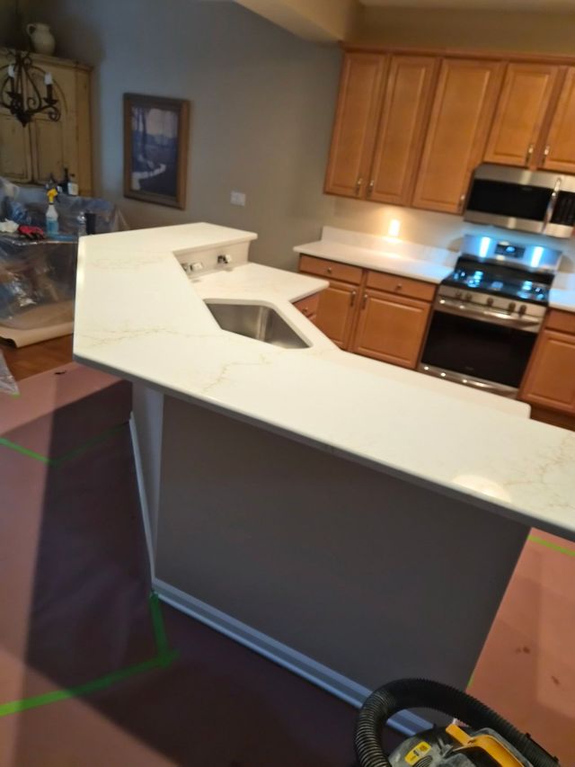 Kitchen with white island countertop, brown cabinets, stainless stove, and a sink cutout in the island.