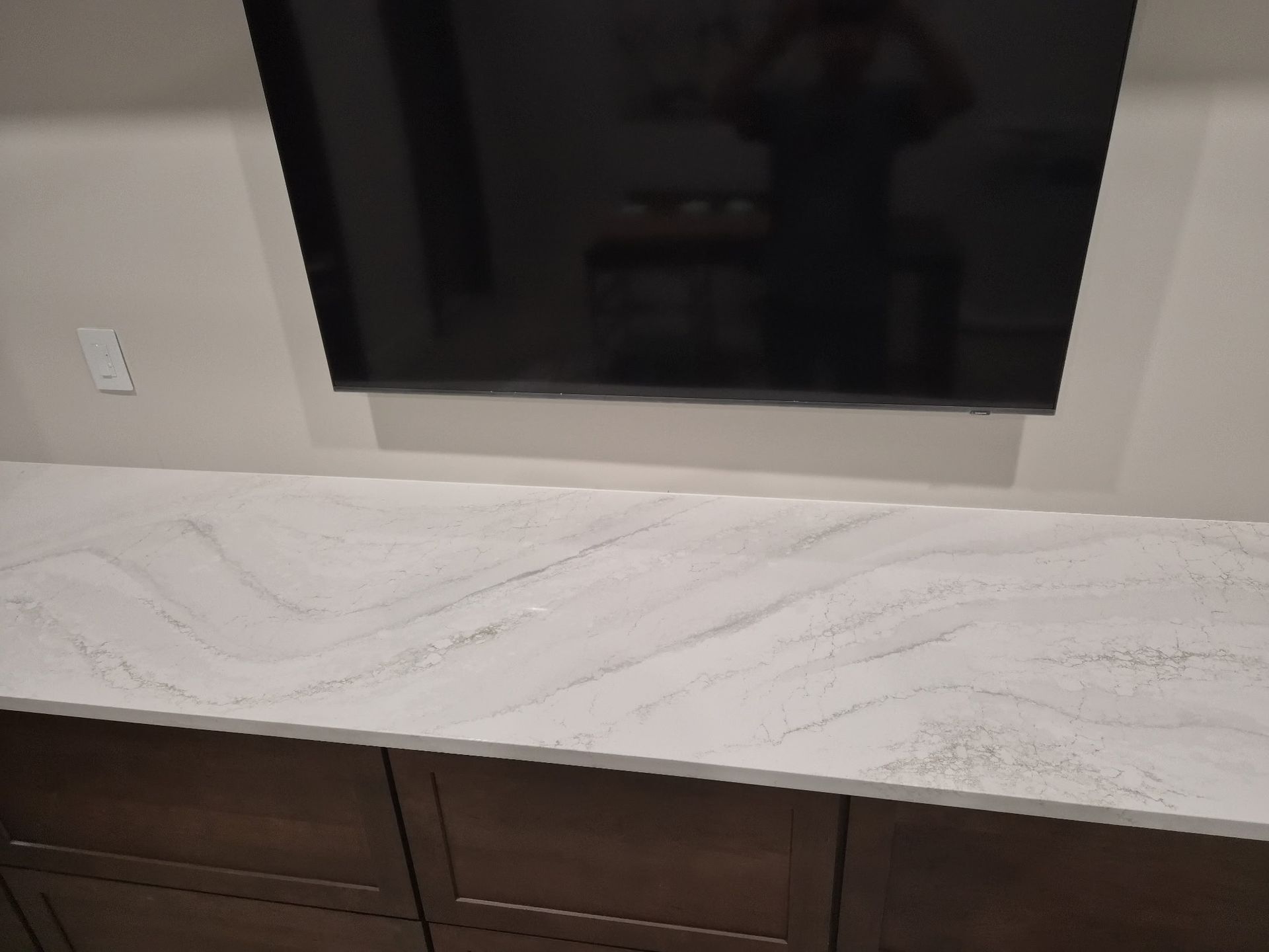 TV mounted above a light marble countertop with dark wood cabinets below