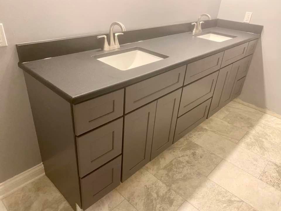 Gray double-sink bathroom vanity with dark countertop and drawers against a light wall