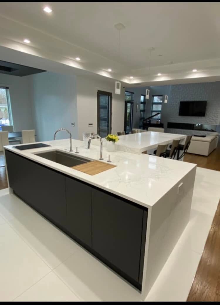 Modern open-plan kitchen and living room with white island, black cabinetry, and wall-mounted TV