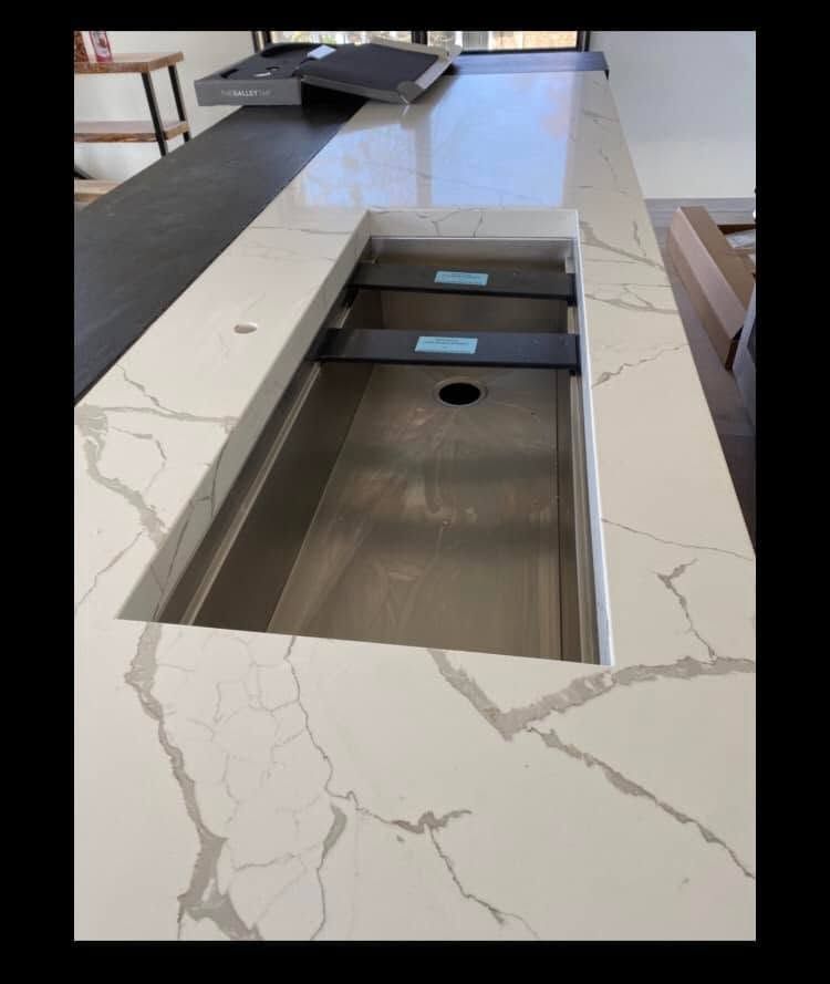 Kitchen island with white marble-pattern countertop and built-in sink opening covered by a metal insert