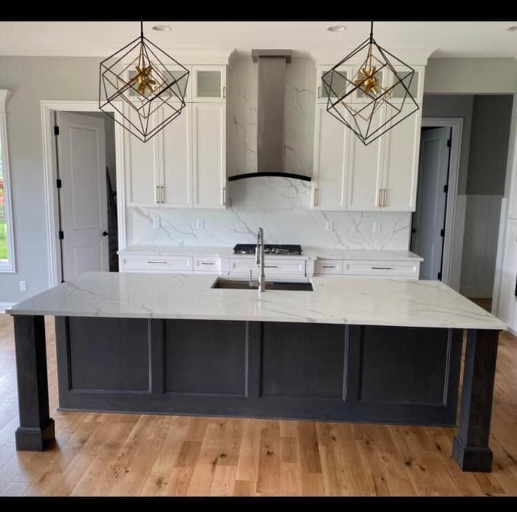 Modern kitchen with dark island, white cabinets, marble countertops, and geometric pendant lights