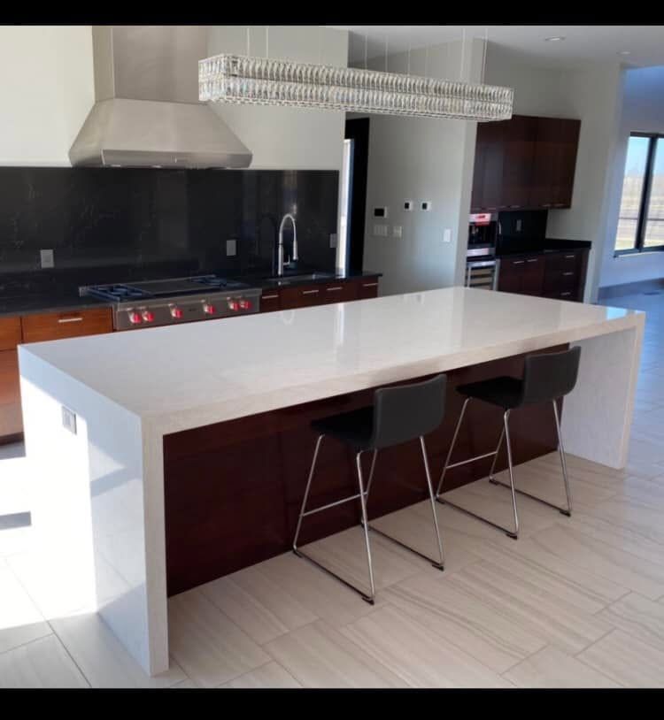 Modern kitchen with large white island, three bar stools, dark cabinets, and pendant lights