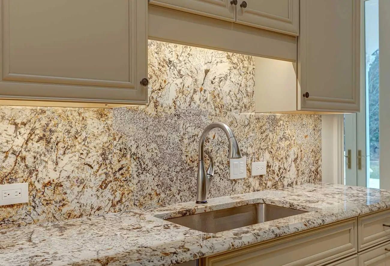 Modern kitchen countertop with granite backsplash, stainless sink, and cream cabinets