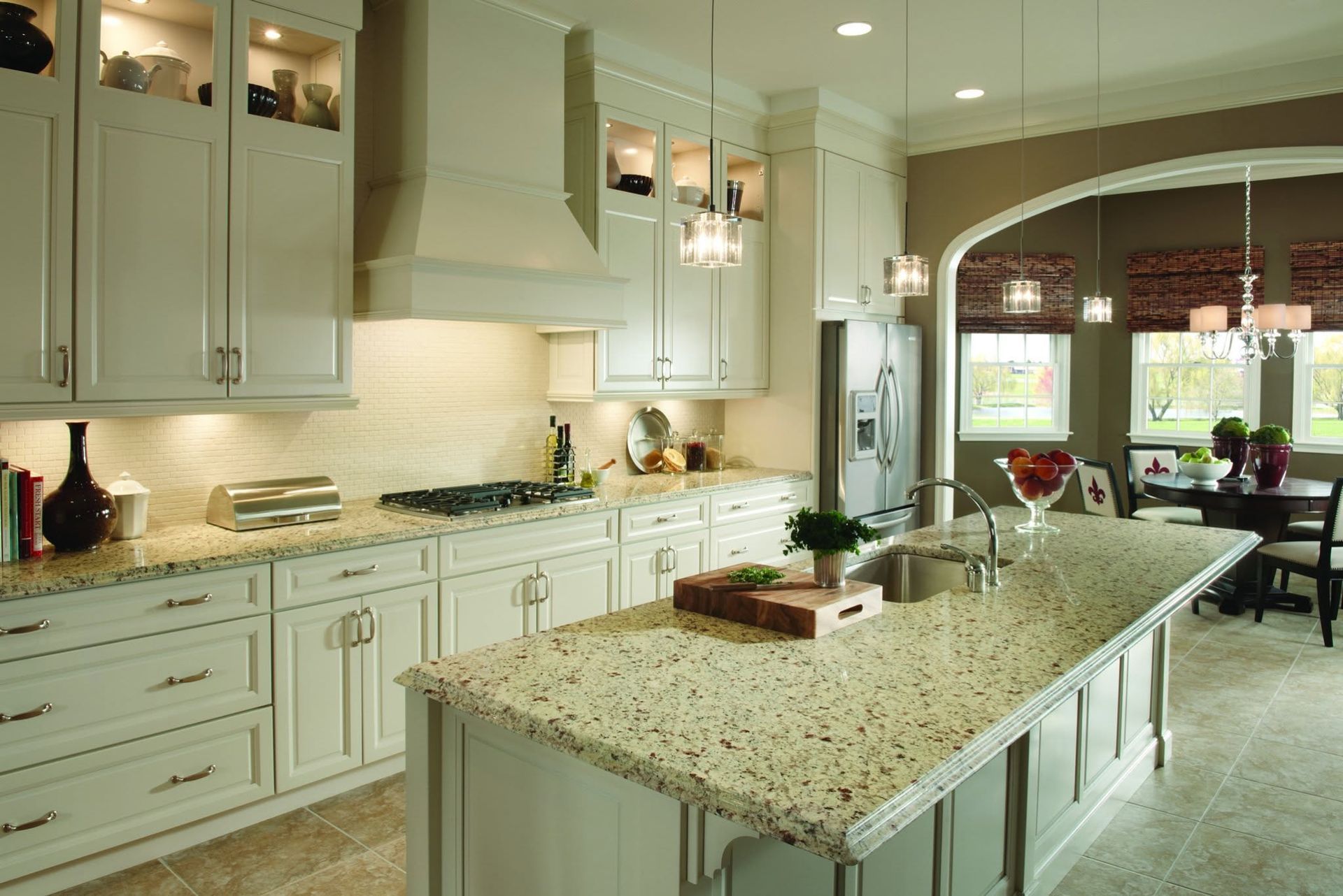 Bright kitchen with pale green cabinets, granite island, and arched doorway to a dining area.