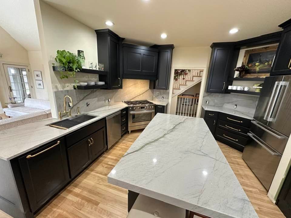 Modern kitchen with dark cabinets, stainless steel appliances, and a large marble island under recessed lighting