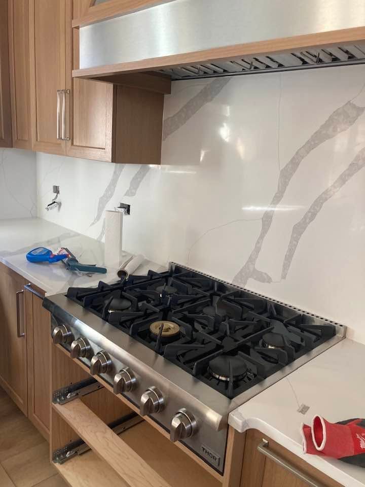 Modern kitchen with gas cooktop, stainless range hood, white marble backsplash, and wood cabinets